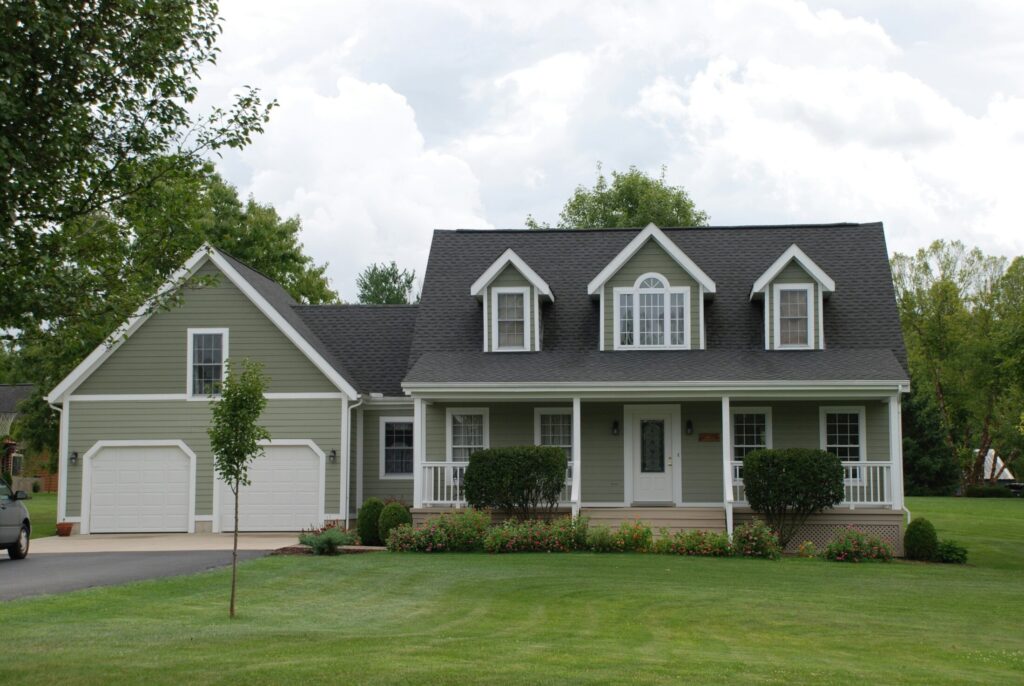 a white and gray house near green grass field with small bushes